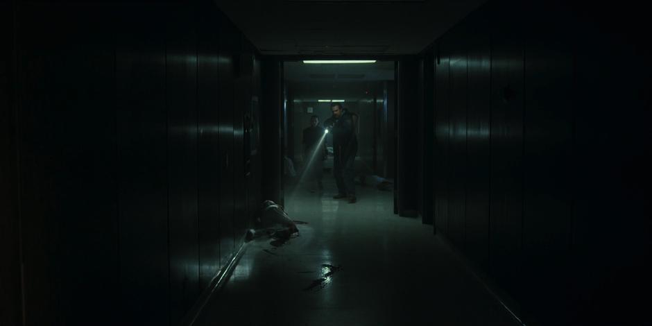 Hopper and Eleven move through the hallway past several dead bodies.