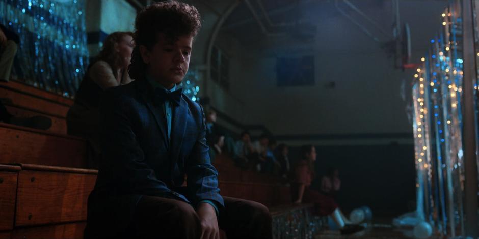 Dustin sits looking sad on the bleachers after getting rejected by several people for a dance.