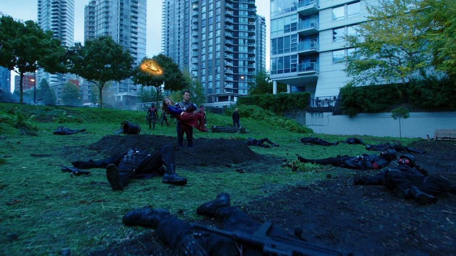 Nate stands with Kara in a crater in the field while several other heroes approach from behind.