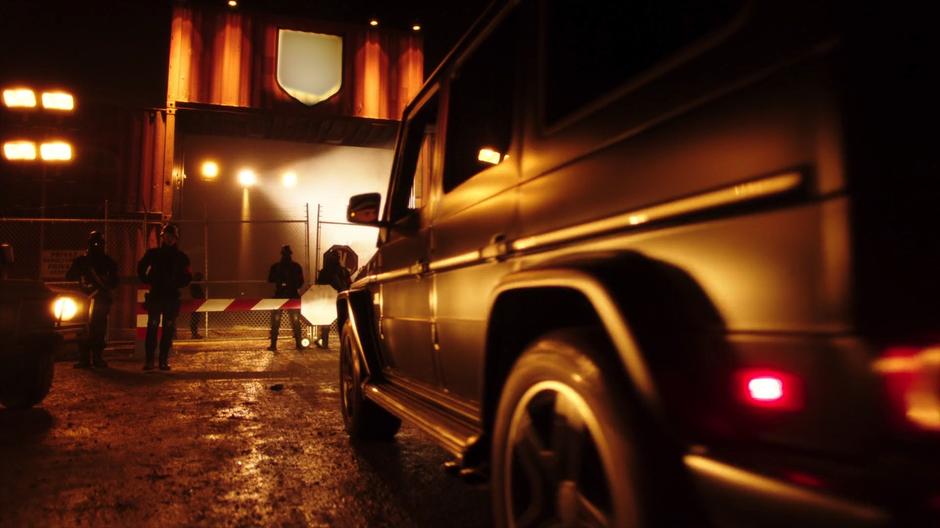 A truck carrying Mick and Oliver drives up to the checkpoint at the gate to the facility.