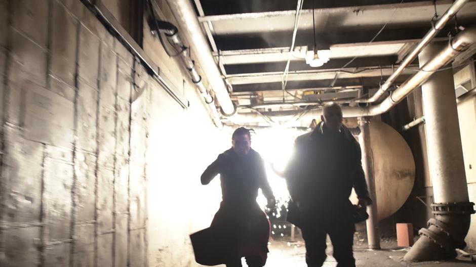 Lena and James run down a hallway as laser blasts spark behind them.