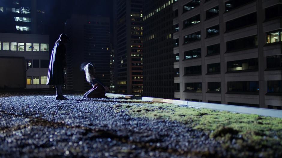 Reign stands over Kara who is kneeling at the edge of the rooftop.