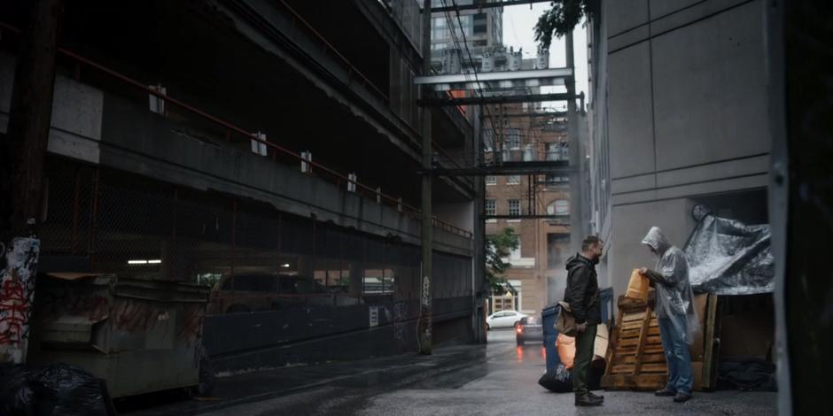 A homeless man looks into the paper bag of money that David just handed him.