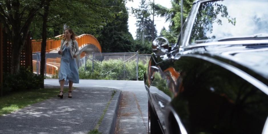 Marcy walks down the street past Luca's car.