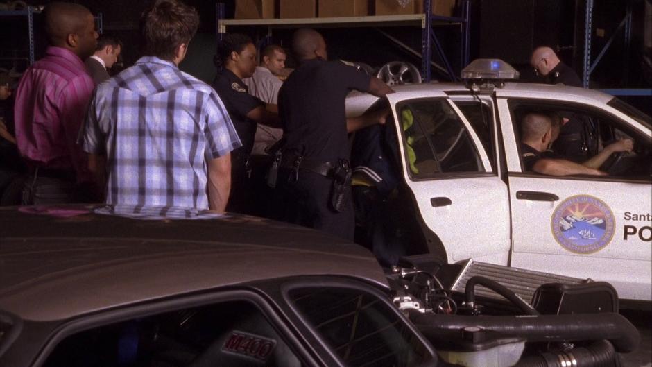 Gus and Shawn watch as the police load Wally in the back of a squad car.