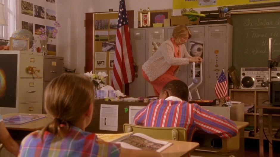 Miss Lepky climbs a step ladder at the front of the class.