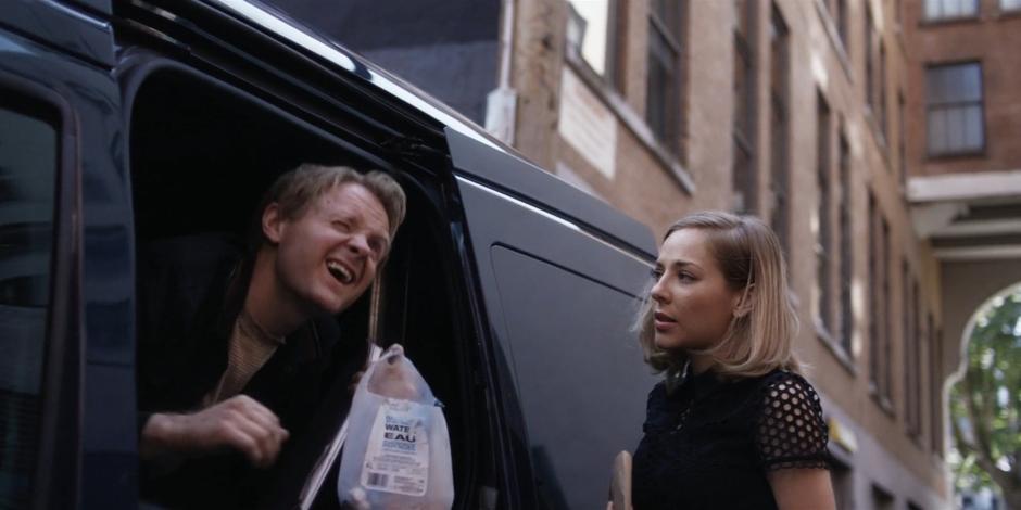 Marcy opens the side door of the van for Simon who squints at the sun.