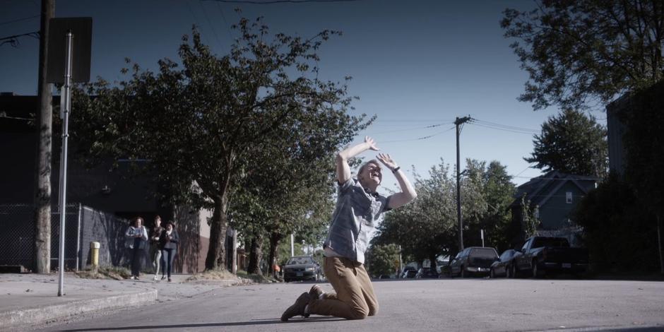 Three people watch Simon as he cowers under the sunlight which he believes is a police spotlight.