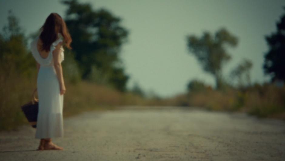 Mary waits by the side of the road in a white dress.