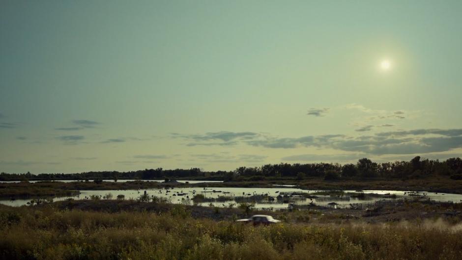 The car drives down the road in front of a small lake.