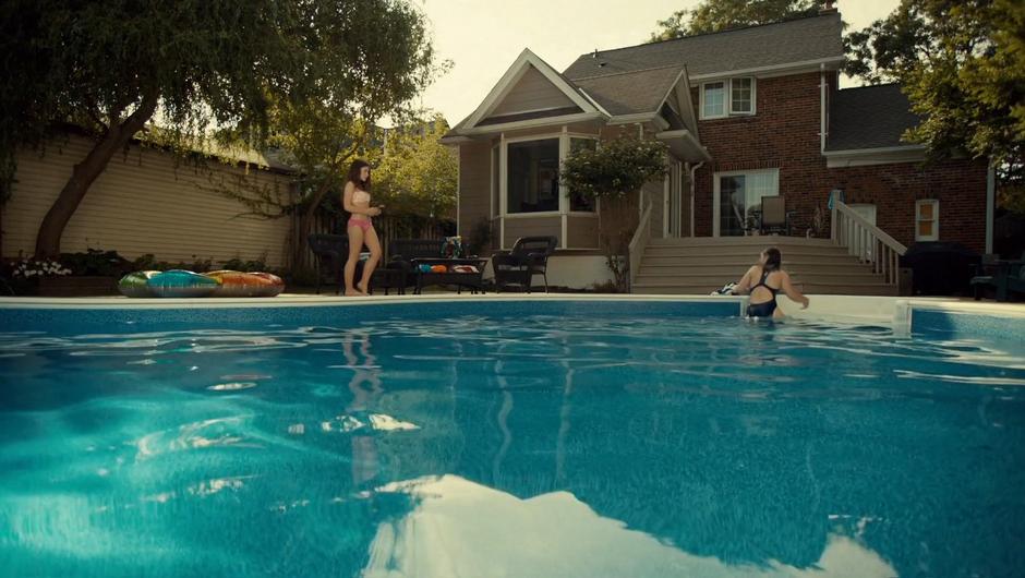 Naomi stands by the pool as Jess climbs out.