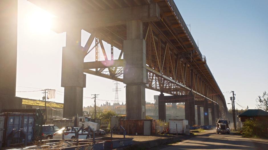 A truck drives down the street under a bridge.