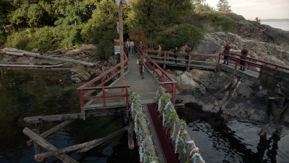 The swordsman walks towards the boat while Margo and Eliot stand on the dock.