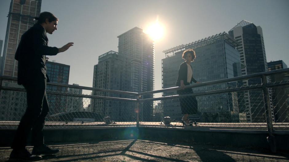 Professor Lipson stands on the edge of the building while Quentin tries to talk her down.