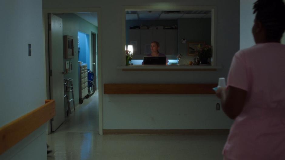 Nurses mill around the nurses station at the end of the hallway.