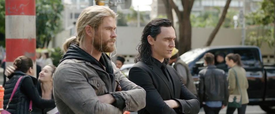 Thor and Loki stand at the corner of the intersection talking.