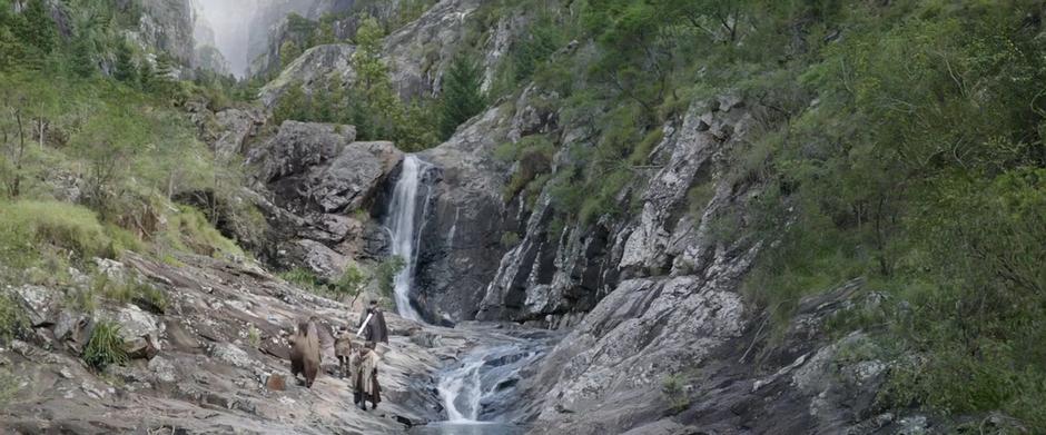 Heimdall leads three refugees up the mountain past the waterfall.