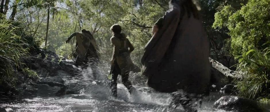 A group of fleeing refugees run down a shallow stream.