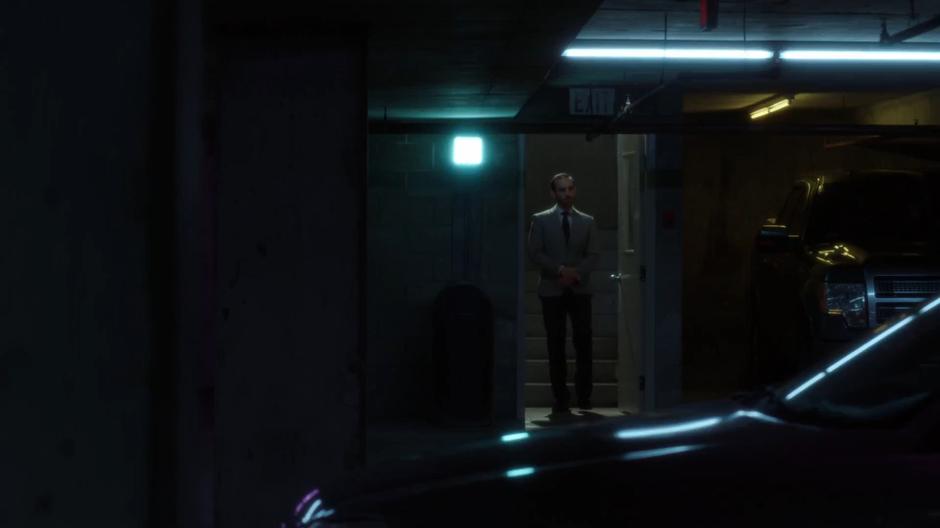 A man in a suit walks down the stairs into the garage.