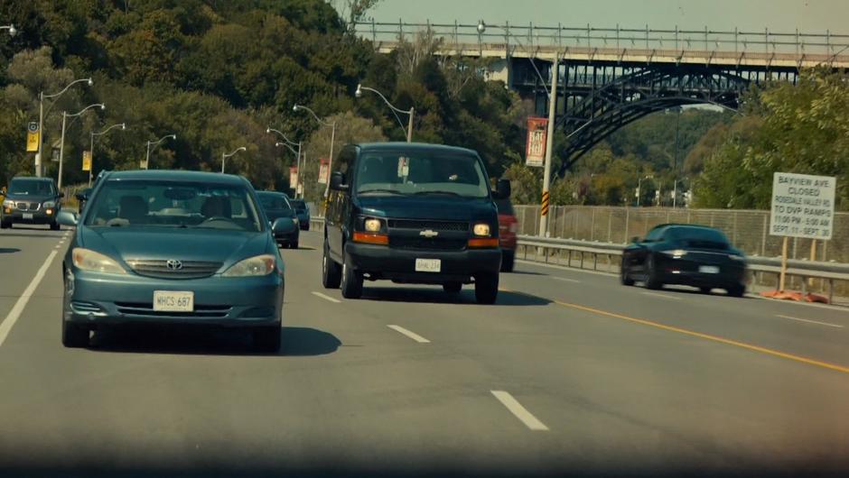 An unmarked black van follows Mary down the road.