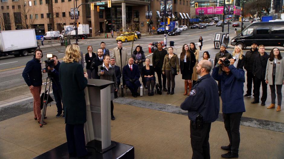 Mayor Van Buren stands on a podium in front of the press introducing the new meta-human-proof building.