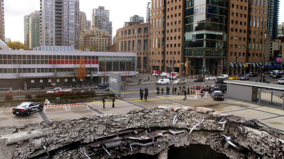 A police line is set up around the giant hole in the ground where the building used to stand.