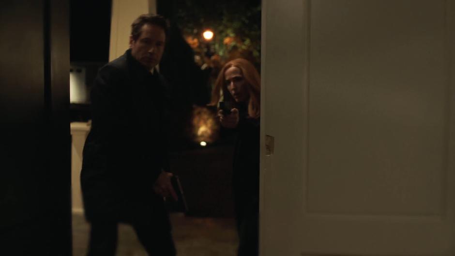 Mulder and Scully burst in through the front door of the house.
