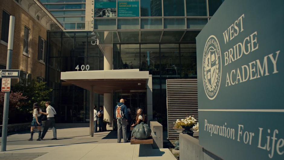 Establishing shot of the front of the school with students milling around.