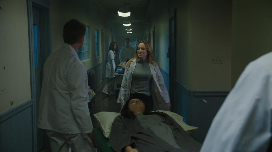 Sara walks up to the doctors who are pushing Nora Darhk on a gurney while the rest of the team waits back in the hallway.