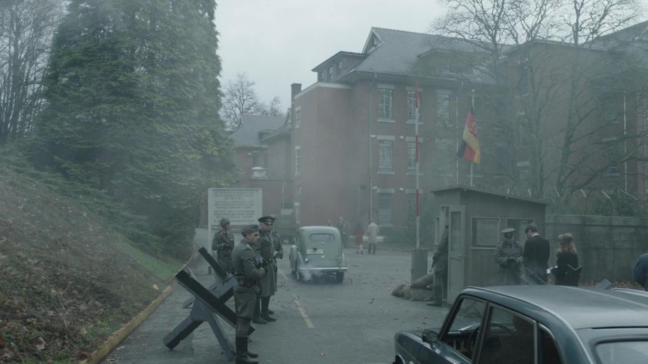 Dr. Vogal drives the car up to the checkpoint as another car drives through ahead of them.