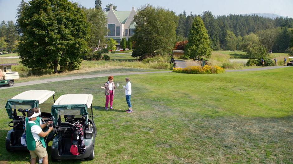 Mrs. Brinks talks to her friend while their caddies prepare their clubs.