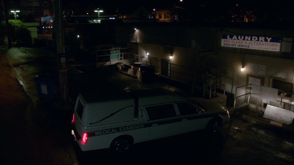 The morgue hearse pulls up behind the laundromat.