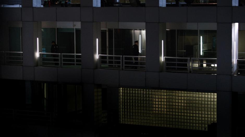 Two police officers patrol the walkway outside the hotel room.