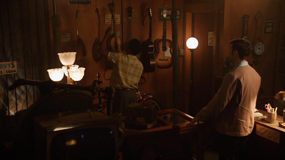 The shopkeeper takes the haunted guitar off the wall while Elvis watches.