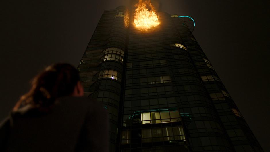 Iris looks up at the building as the fire erupts from one of the upper floors.