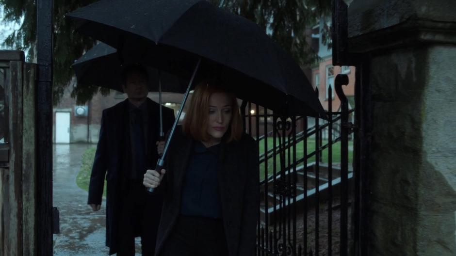 Scully and Mulder walk out to their car while holding umbrellas.