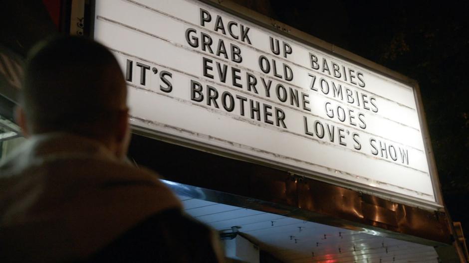 Tucker looks up at the church's sign welcoming zombies.