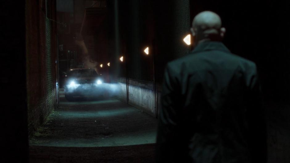 Skinner walks down a narrow alley towards the car.