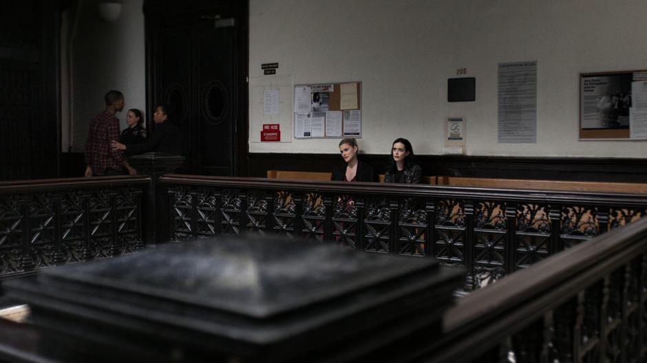 Jessica sits down with Trish in the lobby outside the courtroom.