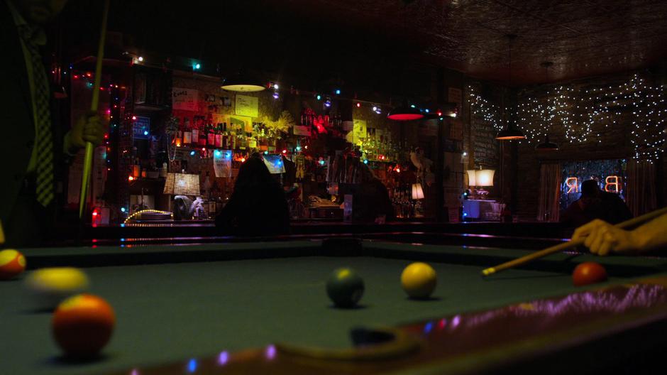 Jessica sits at the bar while someone plays pool in the foreground.