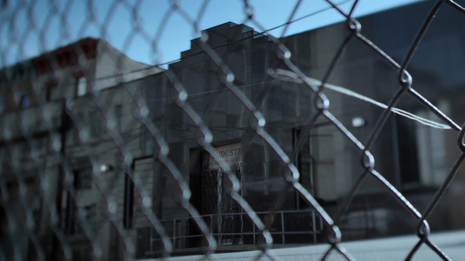 Establishing shot of the building beyond a chainlink fence.