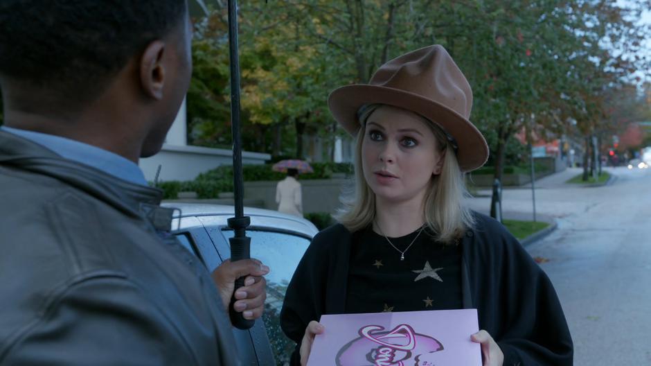 Liv holds up the box of donuts while Clive admires her hat.