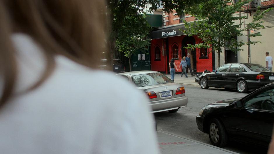 Jessica crosses the street to the bar while Alisa watches from the street corner.