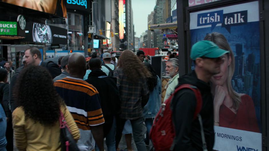 Alisa pushes her way through the crowd past Trish's poster.