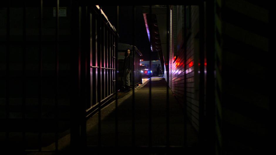 Jessica looks for a way around the police cordon while hiding behind some dumpsters.