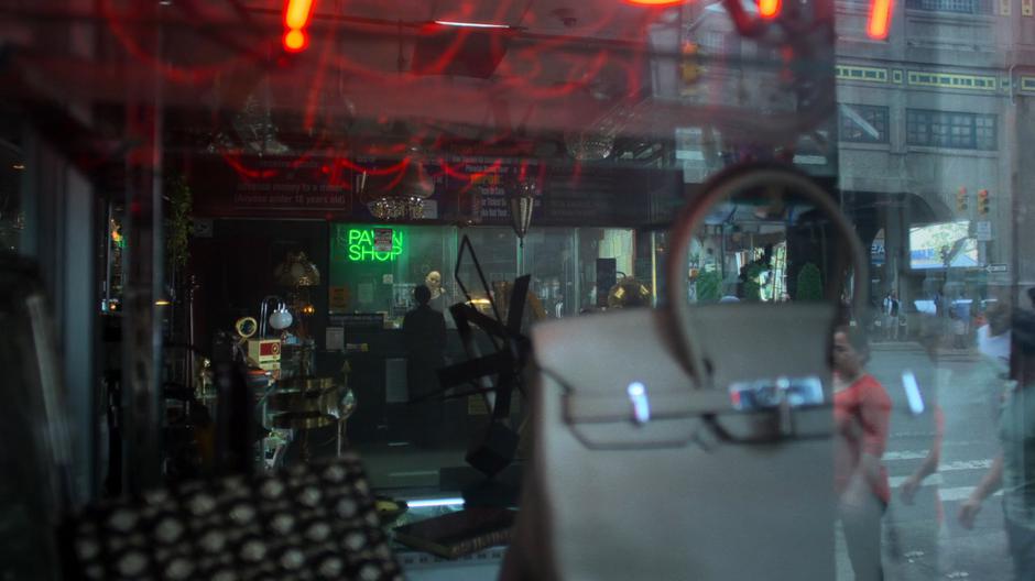 Hogarth talks to the pawn shop employee through the bulletproof glass.