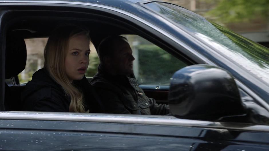 Olivia looks in the side mirror for pursuit after kidnapping Tanya with one of the other cultists.