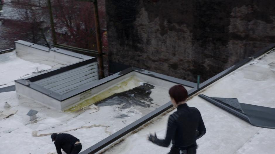 The killer leaps down to a lower part of the rooftop while Alex follows.