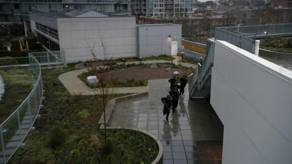 A group of DEO agents run across the rooftop to position.