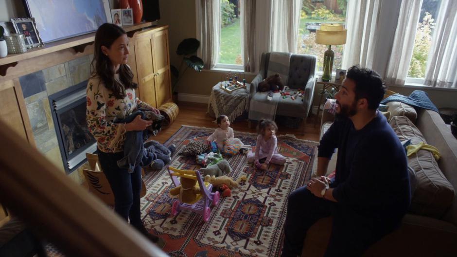 Dave sits down on the edge of the couch and tells Carmen about his plan to take time off of work while their kids play on the ground.